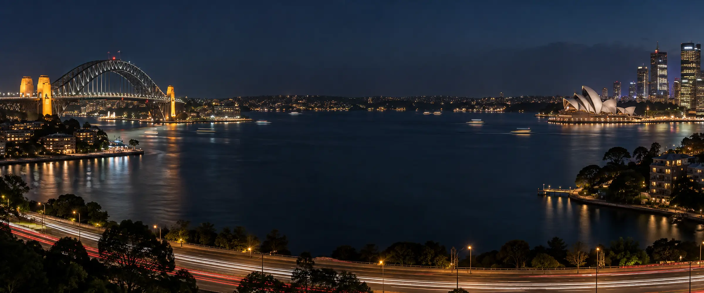 Sydney Harbour and the city skyline at night with car light trails on the road below